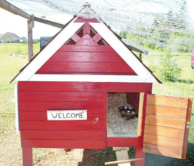 Completed chicken coop with red exterior and welcome sign. 