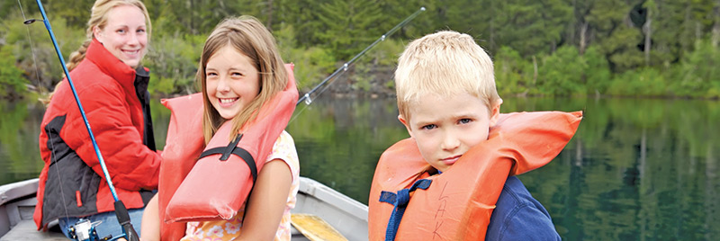 Two children and an adult with life jackets on in a boat fishing.