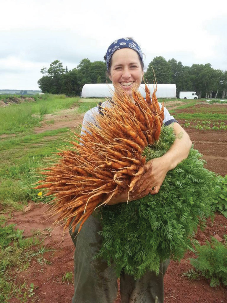 Jen Campbell holding a big bunch of freshly harvested carrots