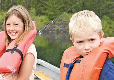 Two children and an adult with life jackets on in a boat fishing.